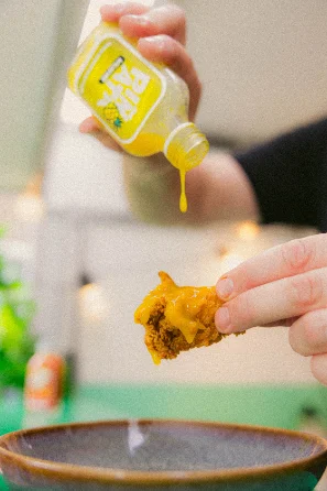 Hot sauce uit het flesje over een stuk kip